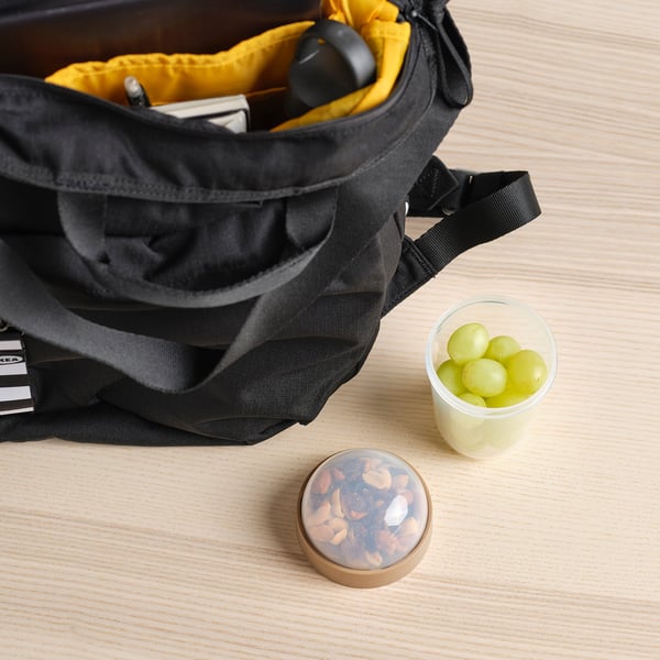 Black backpack open revealing a yellow inside, next to a small container of green grapes and a round container of mixed nuts on a wooden table.