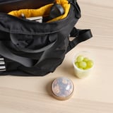Black backpack open revealing a yellow inside, next to a small container of green grapes and a round container of mixed nuts on a wooden table.