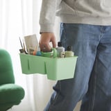 Person carrying green STACKSTOD caddy with art supplies and bottle.