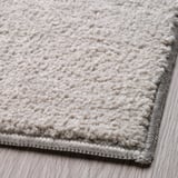 Close-up of soft, textured beige rug with grey border, showcasing quality material and intricate weave.