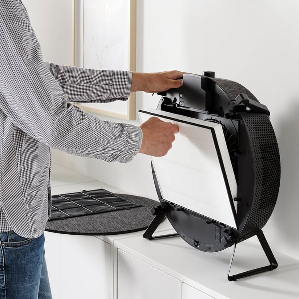 Person installs air purifier filter on a white surface.