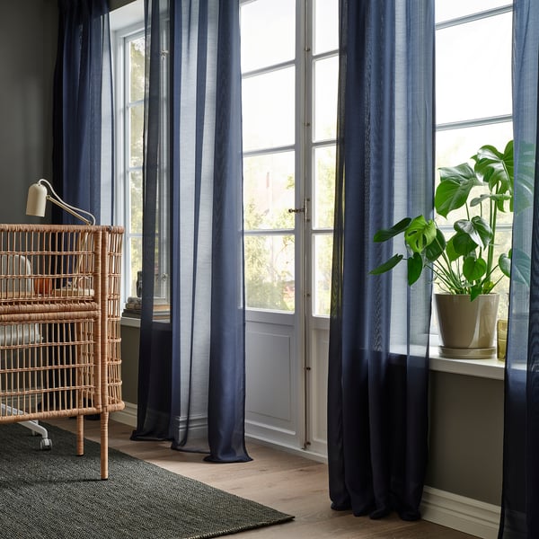 Cozy room with STENFRÖ blue curtains, wicker shelf, and potted plant.
