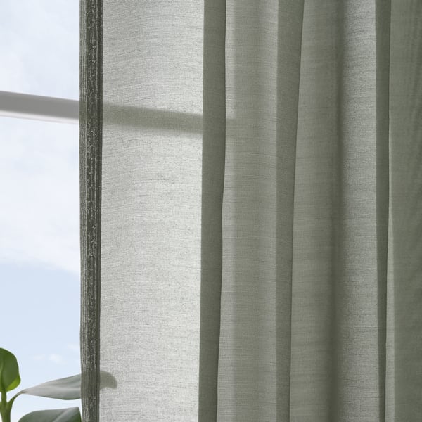 Sheer curtains hang near a window, filtering daylight. Vertical stripes patterns are visible, providing a sense of calm and elegance.