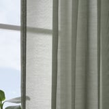 Sheer curtains hang near a window, filtering daylight. Vertical stripes patterns are visible, providing a sense of calm and elegance.