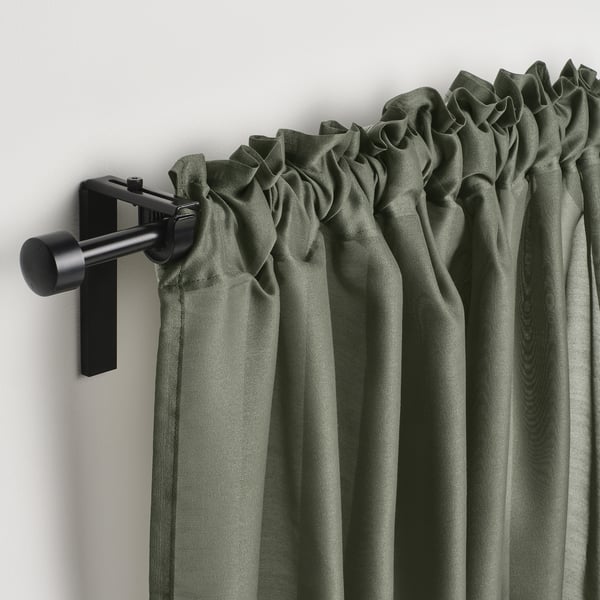 Green curtains hang from black rods, diffusing light and offering privacy with elegant pleats.