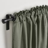 Green curtains hang from black rods, diffusing light and offering privacy with elegant pleats.