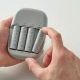 Hand holding battery charger with four ladda 1900 rechargeable batteries, indicating charging process with functional details.