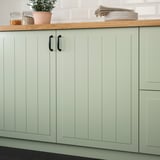 Light green kitchen cabinets with grooved panels and black handles, lacquered for stain resistance and easy cleaning.