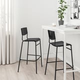 Black STIG stools by white table, modern minimalist design.