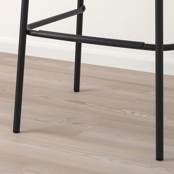 Black metal bar stool legs with footrest on light wooden floor. Sturdy and modern design.