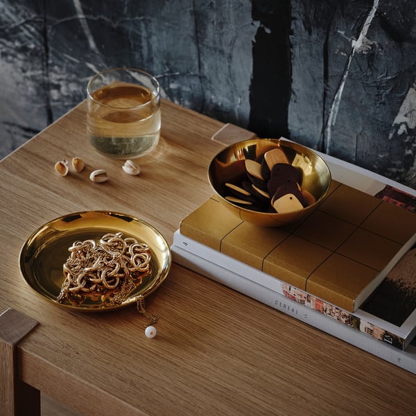 Brass-colored bowl and dish on wooden table, holding jewelry and small decor items. Display and organizing accessories.