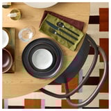 Modern dining setup with dark plates and gold cutlery, olive napkin, on patterned rug.