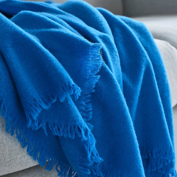 Bright blue throw blanket draped on a white couch, showcasing its soft, plush texture and fringe details.
