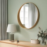 Oak-framed mirror on green wall, reflecting window, with table decor.
