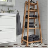 Acacia wood shelving unit in bathroom with towels and toiletries.