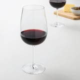Two wine glasses with red wine, cheese, olives on wooden board.