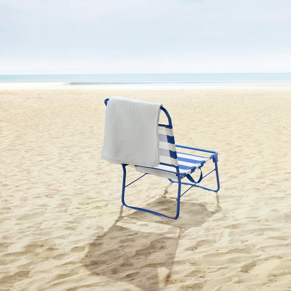 STRANDÖN beach chair on sand, ocean waves in distance, towel hanging.