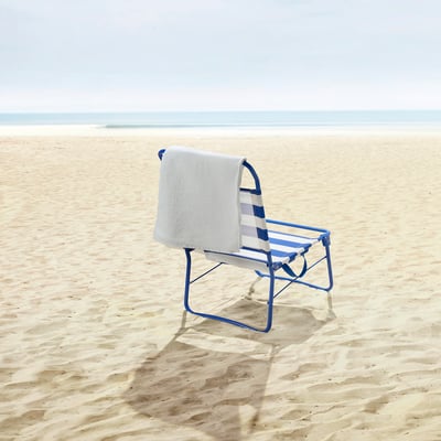 STRANDÖN beach chair on sand, ocean waves in distance, towel hanging.