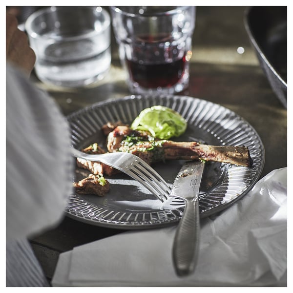 Black paper plate with brown food, a fork and knife on table beside glasses.