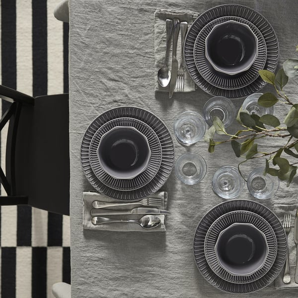A fine dining setup with gray plates, cutlery, and glasses arranged on a gray tablecloth.