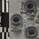 A fine dining setup with gray plates, cutlery, and glasses arranged on a gray tablecloth.
