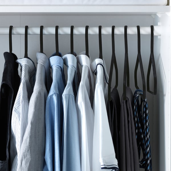 Closet with black velvet hangers holding neatly arranged blue and black clothes.