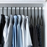 Closet with black velvet hangers holding neatly arranged blue and black clothes.