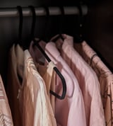 Black hangers with velvet coating, neatly holding pink and beige clothes.