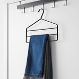 Black trouser hanger with hook, holding three folded jeans on white shelf.