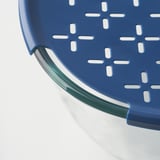 Blue plastic colander with green handle and cutout design.