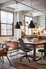 Modern dining area with black SVARTNORA pendant lamps, wooden table, and colorful chairs. Large window and open kitchen in the background.