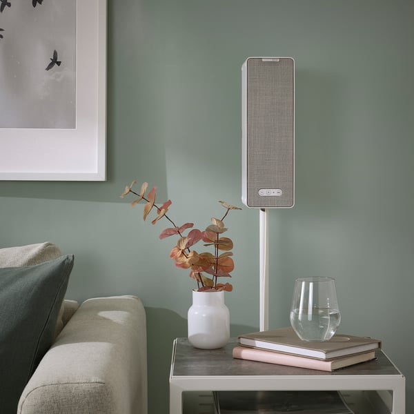 Clear floor-standing speaker near green sofa, with vase & glass.