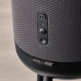 Close-up of sleek, black speaker with fabric cover, featuring play/pause and volume controls, showcasing high-quality design.