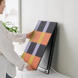 A person is attaching a colorful panel to a SYMFONISK wifi speaker, showcasing its customizable design feature.