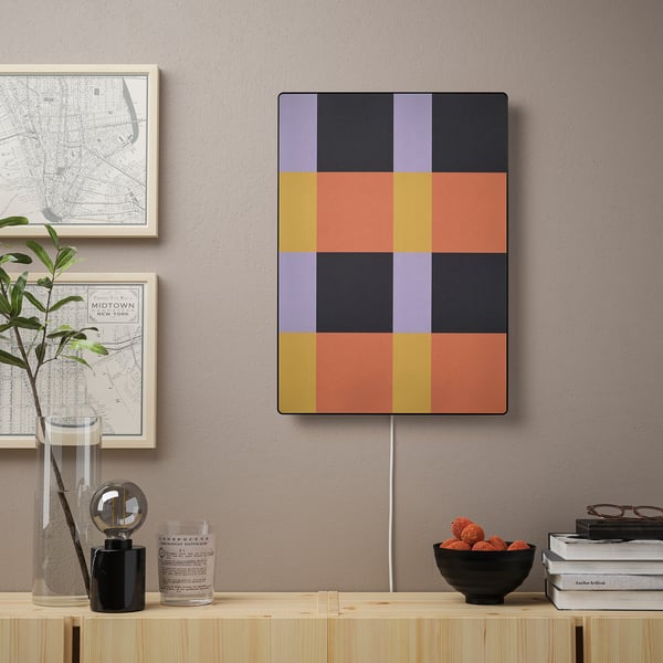 Colorful geometric art panel hangs on wall, part of SYMFONISK wifi speaker, beside decorative items.