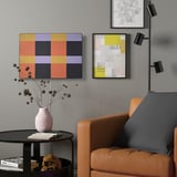 SYMFONISK wifi speaker on gray wall with art, beside brown leather chair.