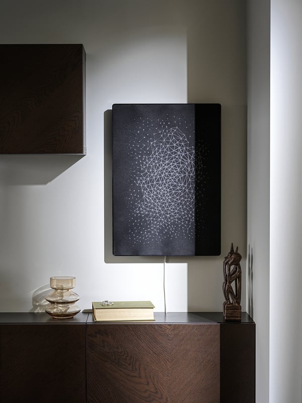 Modern room with SYMFONISK speaker, wall-mounted above wooden furniture, decorated with bowl, book, and sculpture.
