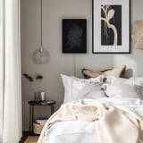 Modern bedroom with white bedding, hanging light, and wall-mounted black speaker-frame combo.