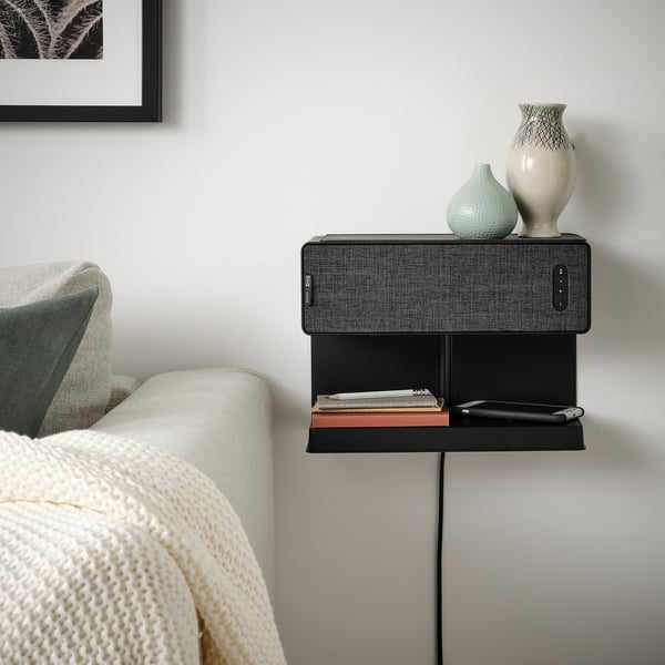 Modern bedroom setup: black SYMFONISK speaker on wall, small, sleek, beside cozy bed.