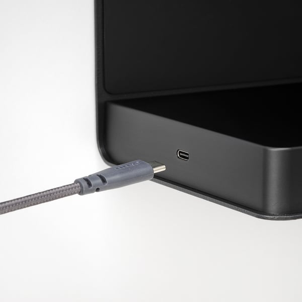 Black speaker connected to gray charging cable, plugged into usb port.