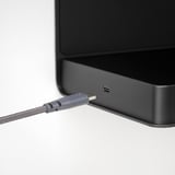 Black speaker connected to gray charging cable, plugged into usb port.