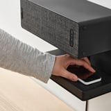 Person placing phone on wireless charger under speaker.