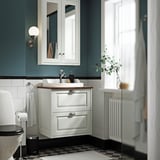 Wall-mounted TÄNNFORSEN vanity, semi-recessed basin, black & white floor, tall radiator, teal walls, greenery.