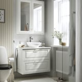 Modern bathroom with TÄNNFORSEN vanity, mirror cabinet, and radiator. Flowers on shelf. Elegant design.