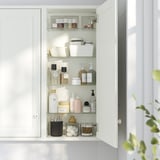 White bathroom cabinet with adjustable glass shelves, storing beauty and skincare products.
