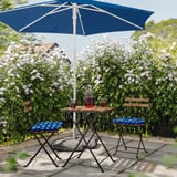 Outdoor patio set with blue table, chairs, and cushions under a blue umbrella, surrounded by white flowers.