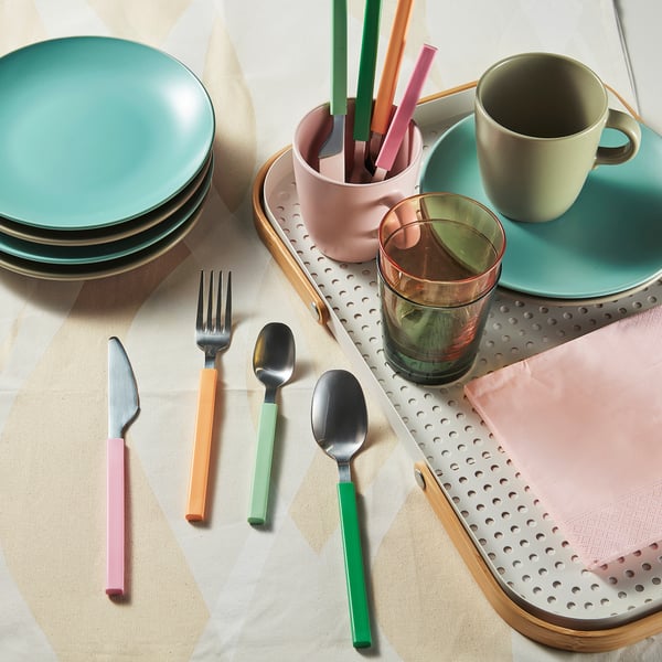 Colorful cutlery set on a perforated tray, with plates, cups, and glasses. Forks, knives, spoons, and teaspoons are neatly arranged, ready for use.