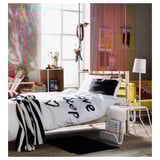Modern bedroom with white TARVA bed, black & white linens, striped blanket, colorful decor, wide windows, shelves, and a desk by the window.