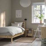 Minimalist bedroom with TARVA light pine bed, white bedding, wooden nightstand, and potted plant by window.