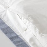 Close-up of white button on folded white duvet cover, showing its smooth texture and functional design.